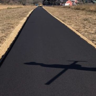 Black asphalt driveway leads to a house; the shadow of an airplane falls on it.