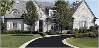 Stone house with curved black driveway and manicured lawn.