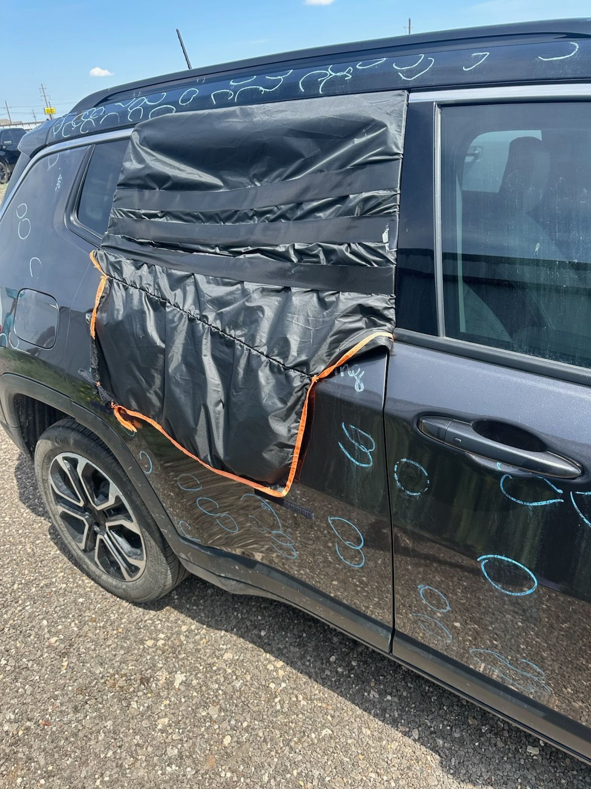 Black SUV with a taped-over damaged rear side window and door, parked on gravel in daylight
