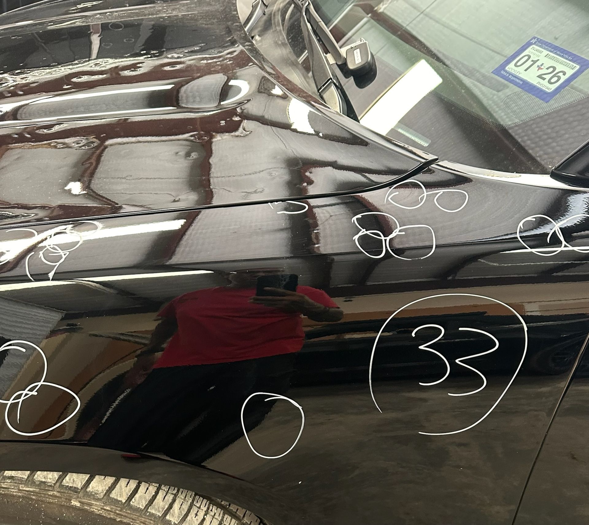 Black car hood and windshield with multiple paint dents and white inspection markings.