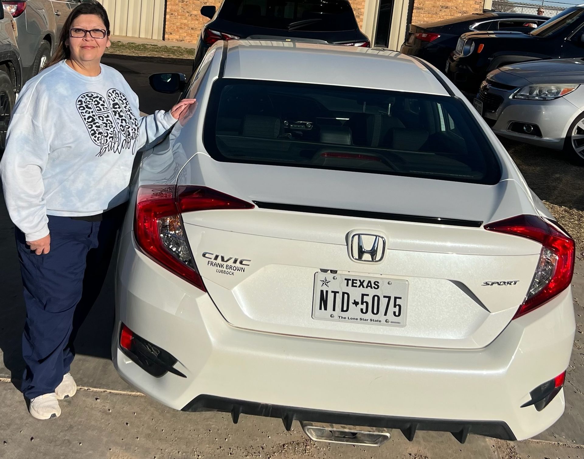 Person standing beside a white Honda Civic with Texas plates in a parking lot.