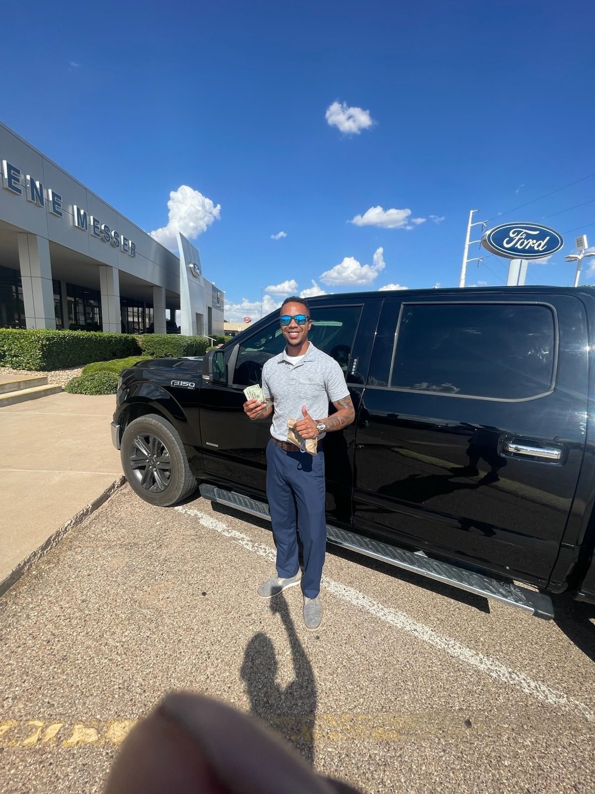 Man standing beside a black pickup truck outside a dealership on a sunny day