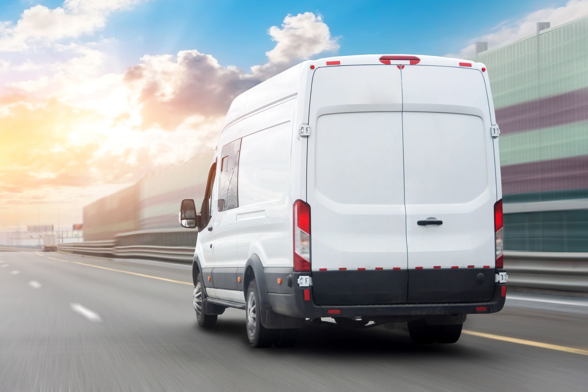 White cargo van driving on a city highway at sunset, rear view