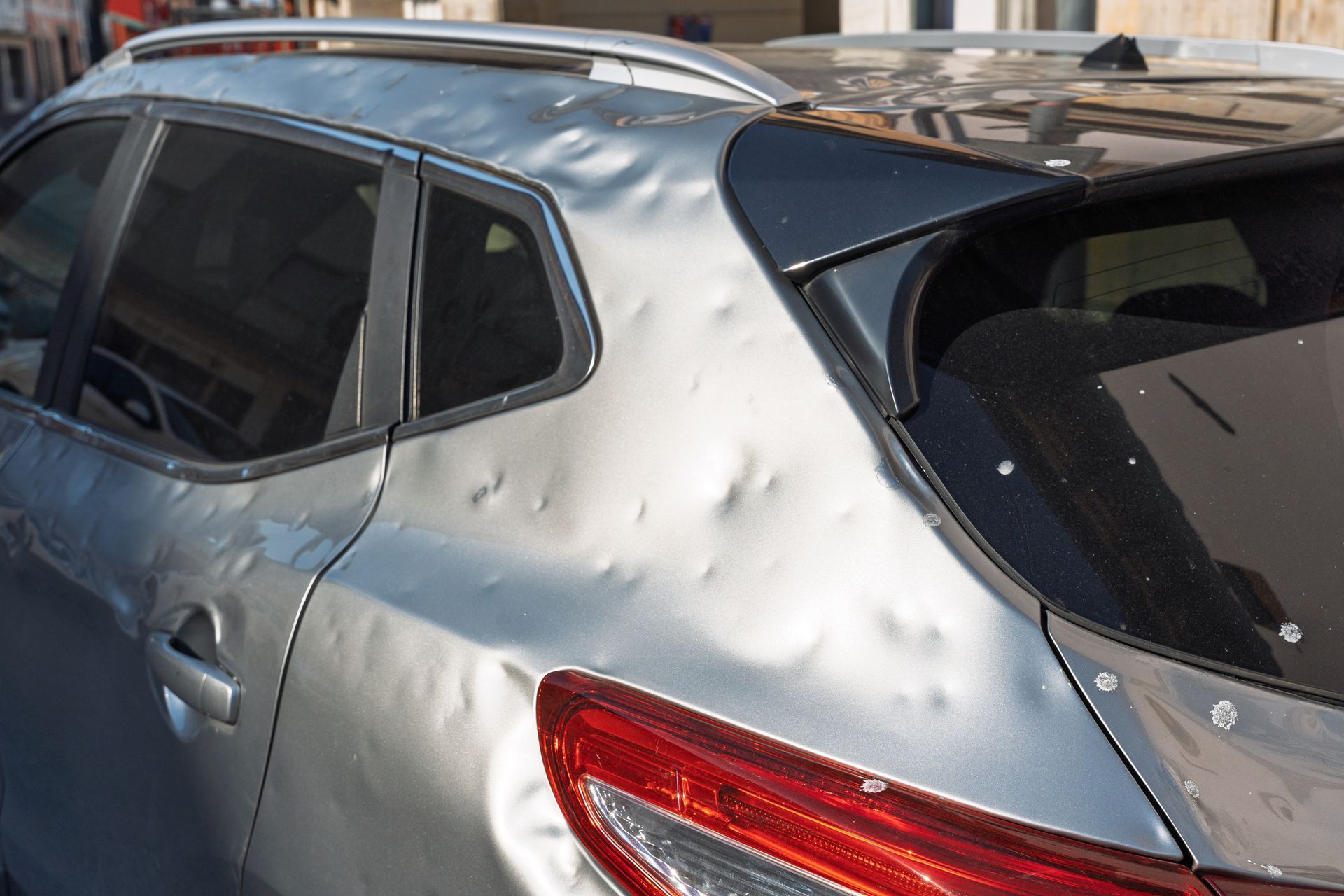 Silver car with large dents and damage on the rear side panel and roof area.