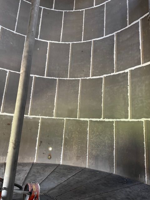 Inside of a large, cylindrical tank, possibly a silo. Dark gray rectangular panels with white caulking form the walls.