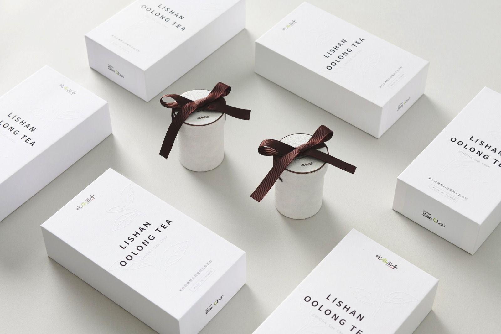 Minimal product display with white boxes and two small gift jars tied with brown ribbons on a light background