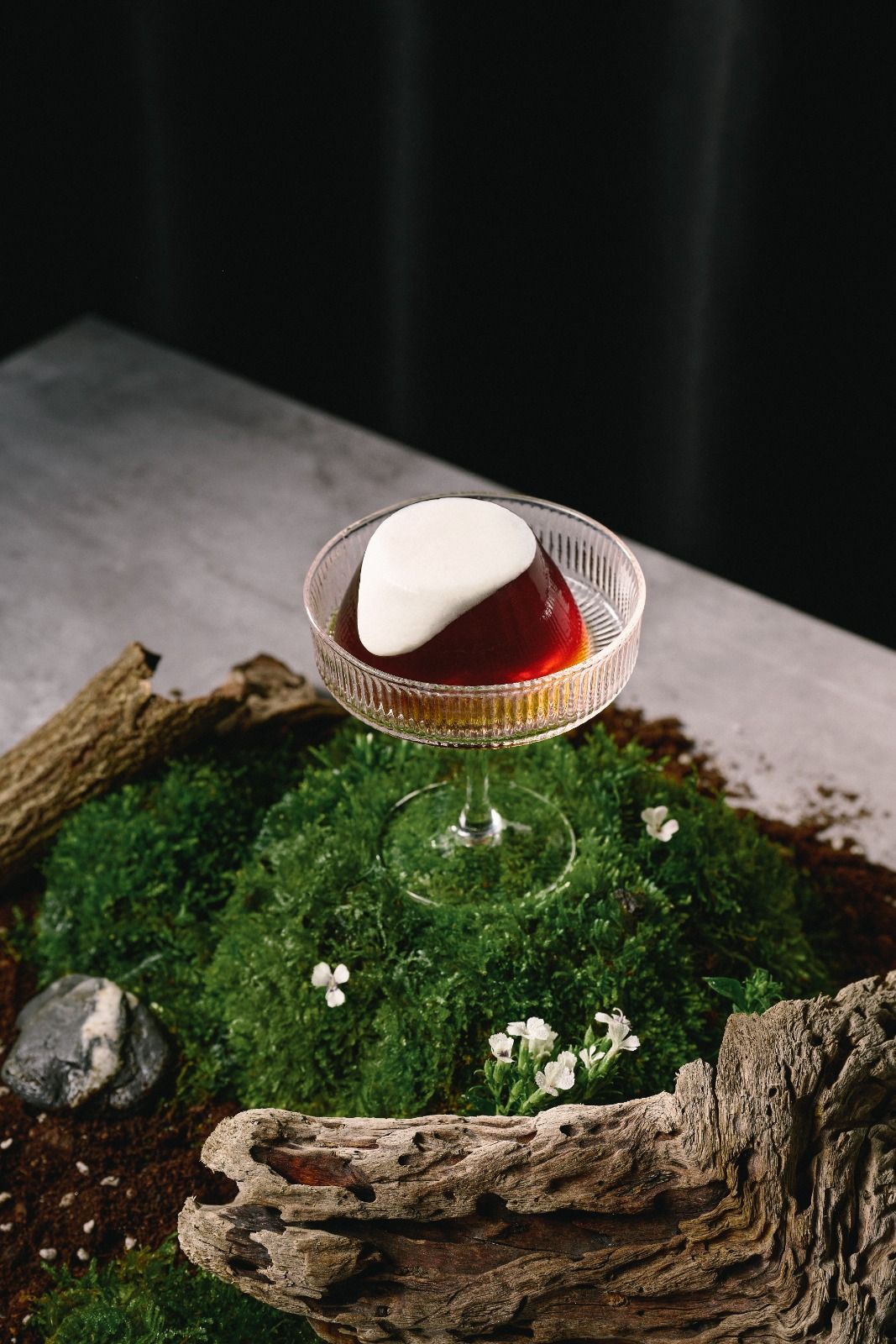 Glass dessert dish with amber liquid and white scoop on moss in a rustic bark planter