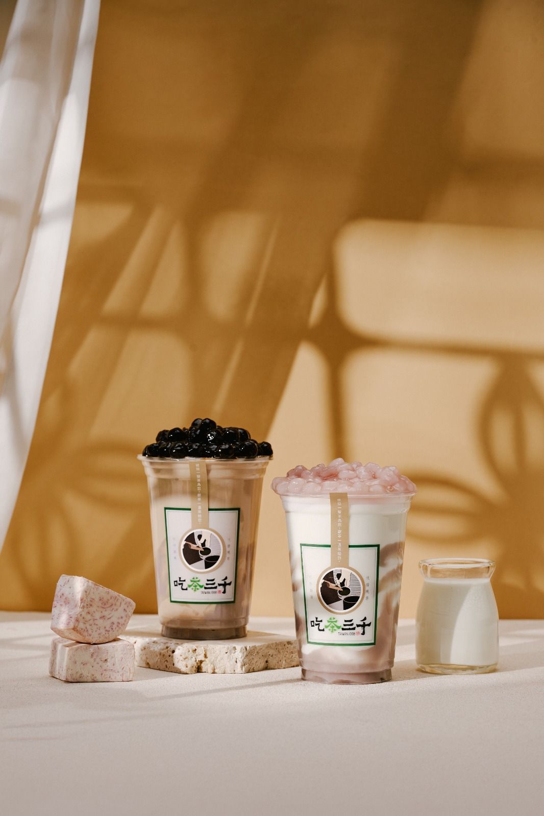 Two iced drinks and a small milk bottle on a white table against a warm beige backdrop.
