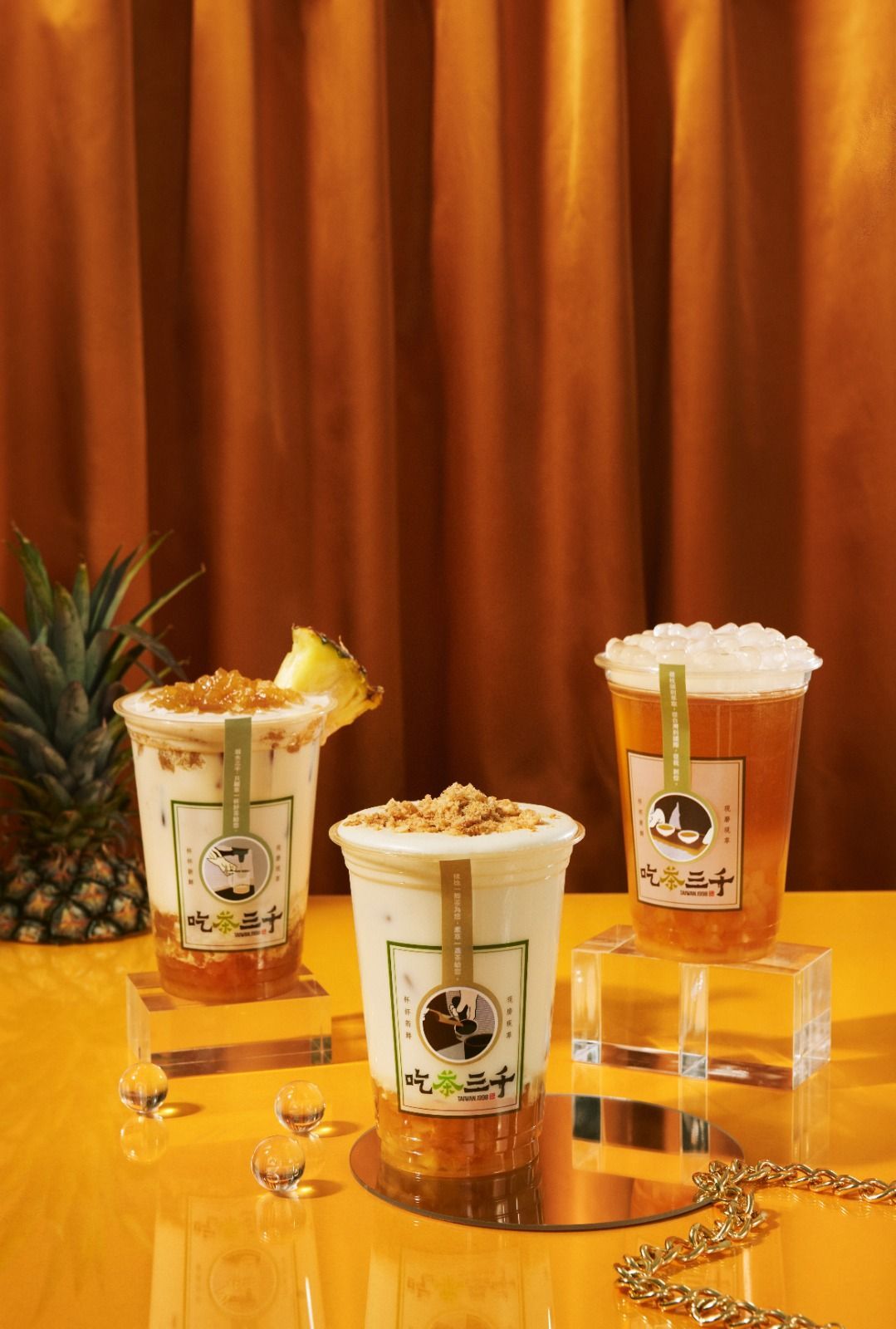 Three tropical cocktails on a gold table with pineapple garnish and orange curtain backdrop