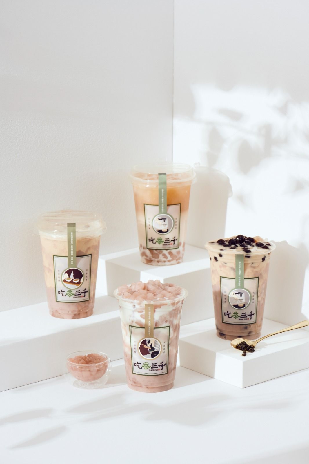 Four iced coffee drinks on white blocks in soft daylight, with whipped cream and chocolate drizzle
