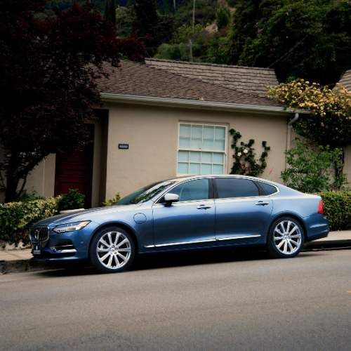 A blue car is parked on the side of the road in front of a house