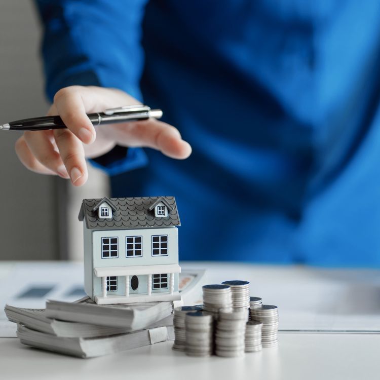 a person is holding a pen next to a model house and stacks of coins .
