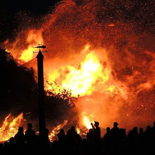 A group of people are standing in front of a large fire.