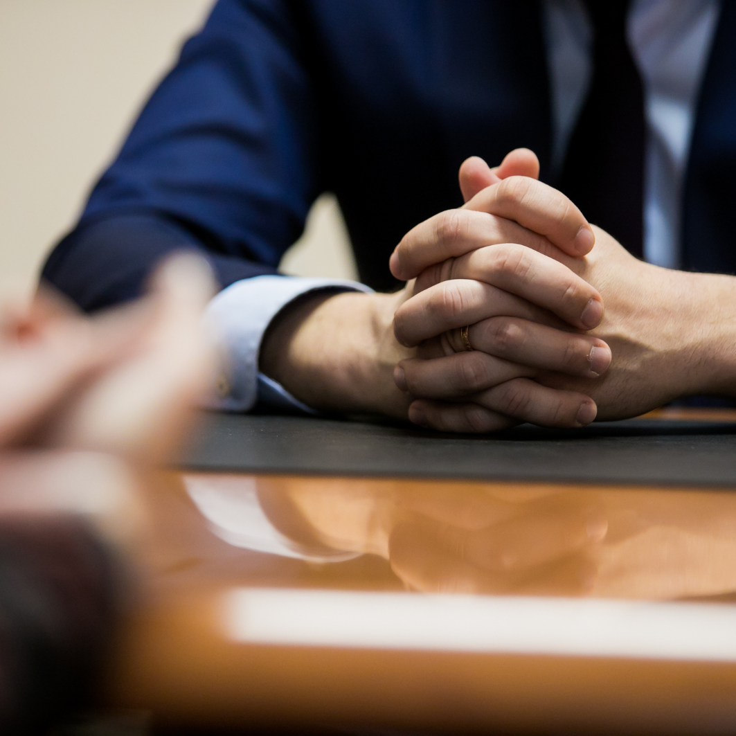 A man is sitting at a table with his hands folded