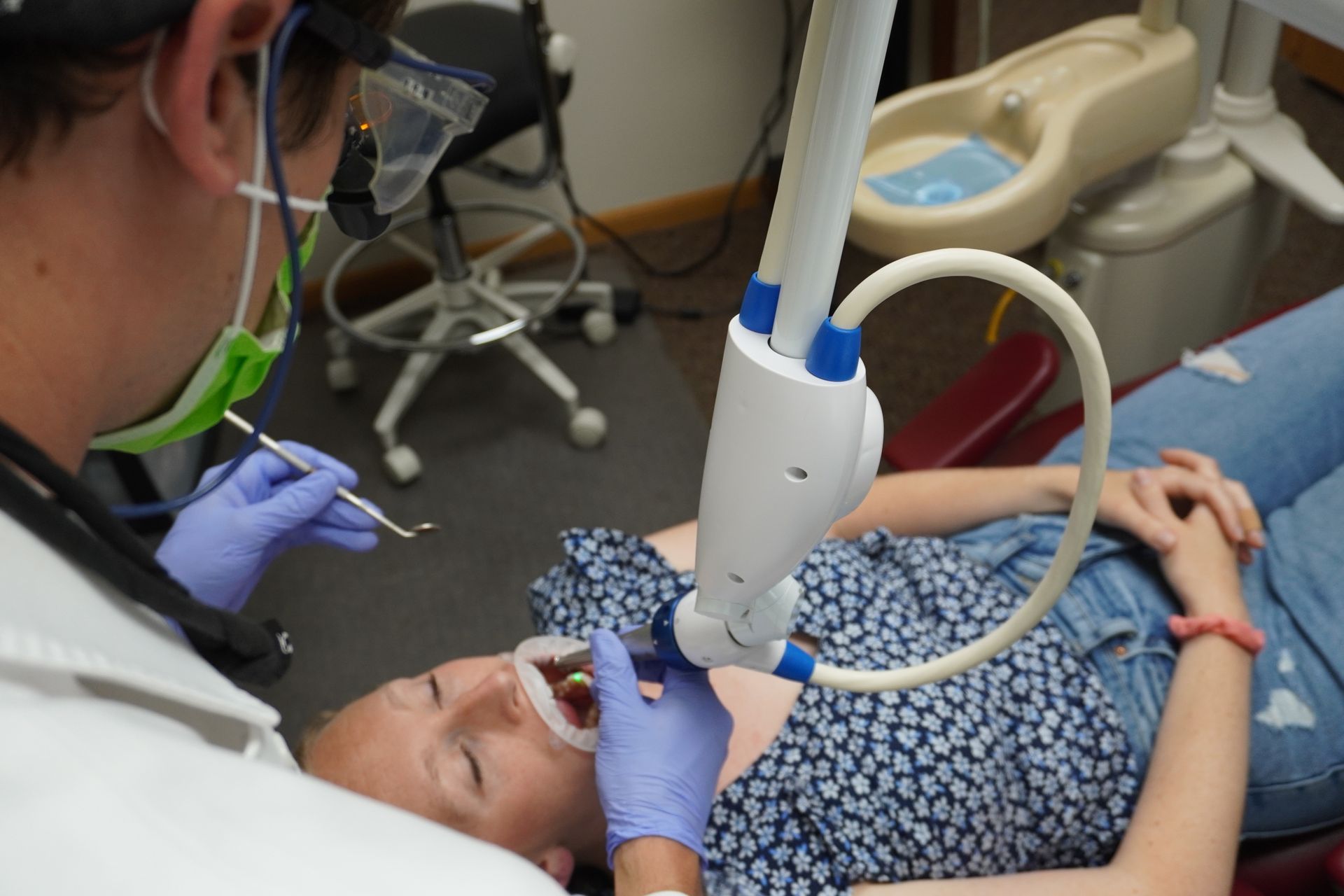 Dentist examining a patient's mouth with tools and a dental light in a dental office.