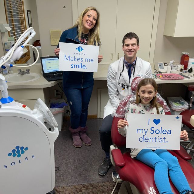 Dentist, patient, and woman hold signs in dental office. 
