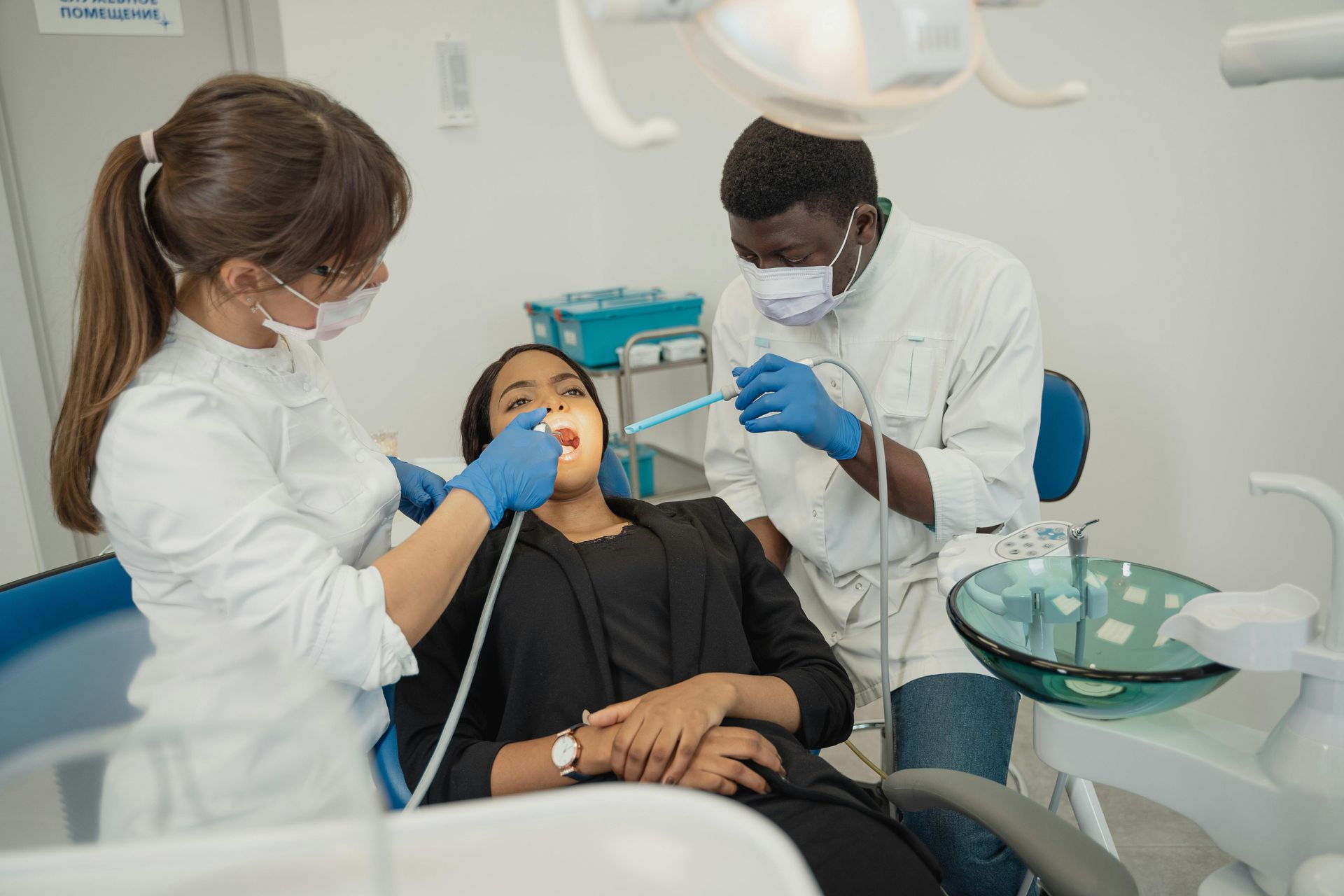 Dentist and assistant examine patient's mouth with tools in a dental office.
