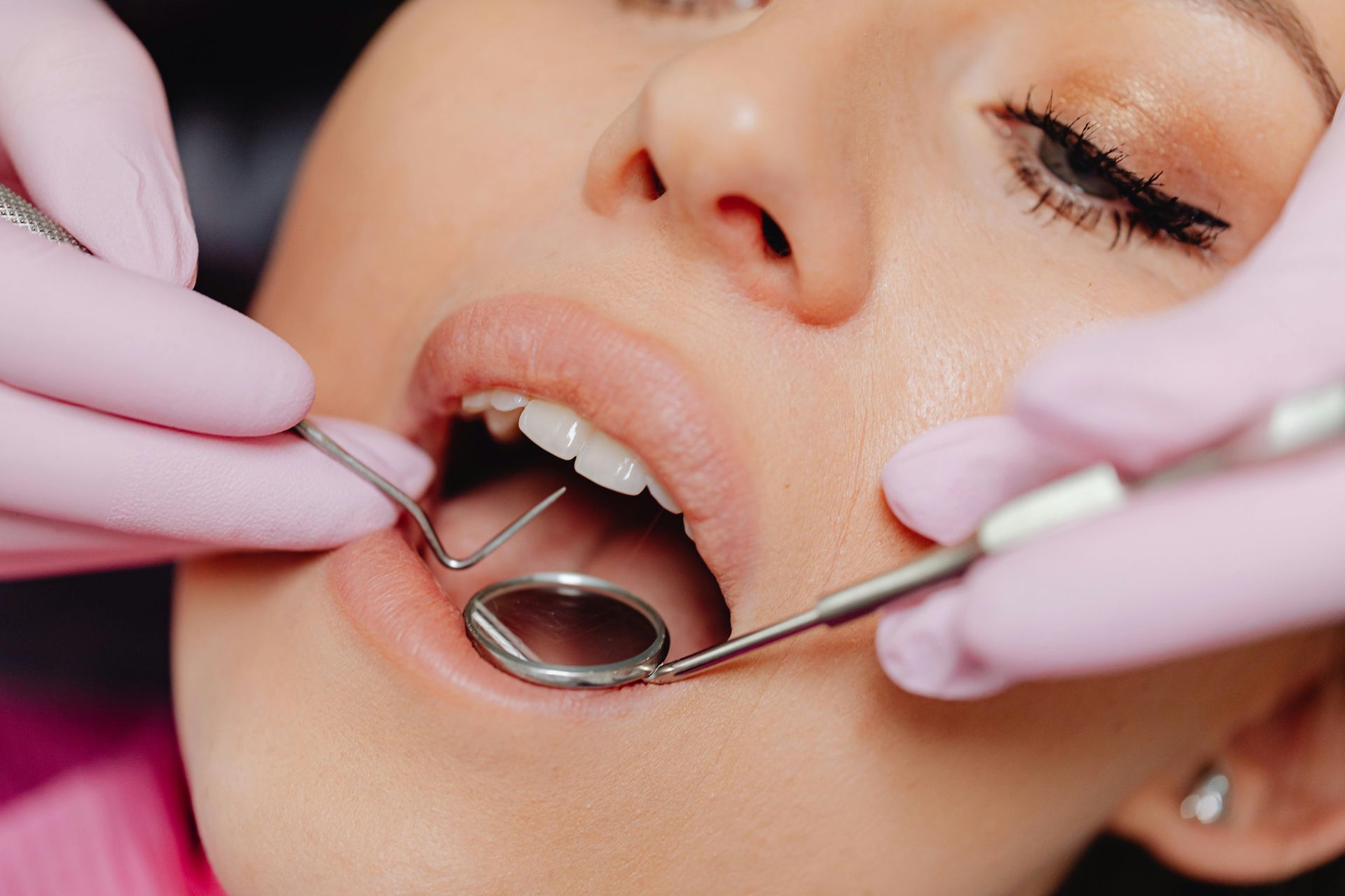 Woman at dentist, mouth open, receiving examination. Pink gloves, dental tools, close-up.