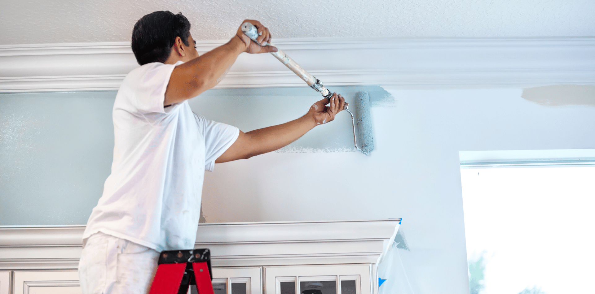 A man is painting the ceiling of a room with a paint roller.