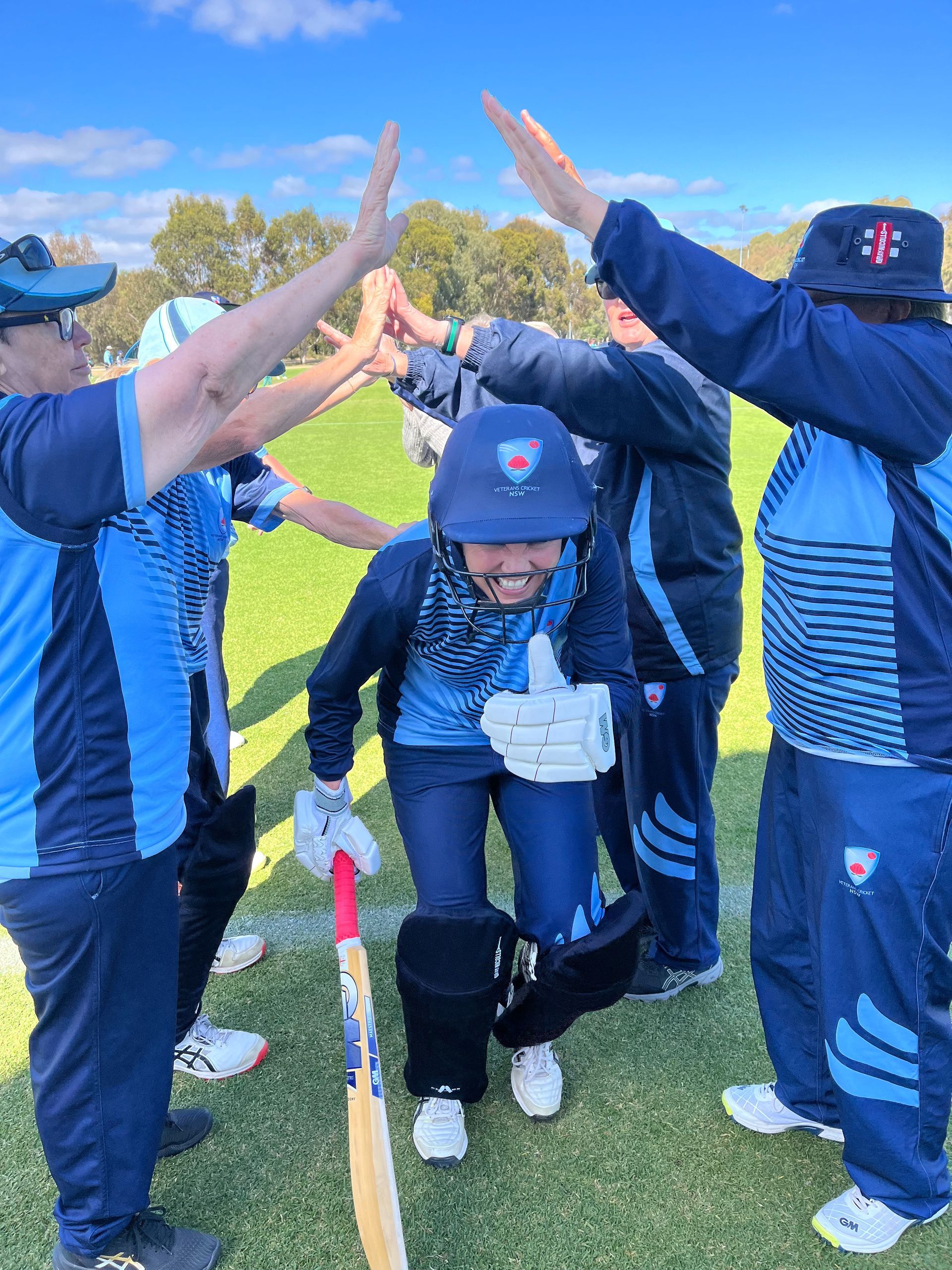 Cricket team in blue and light blue uniforms celebrates, giving high-fives after a game
