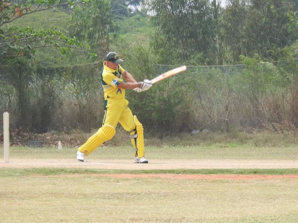 Cricket player in yellow uniform swings a bat