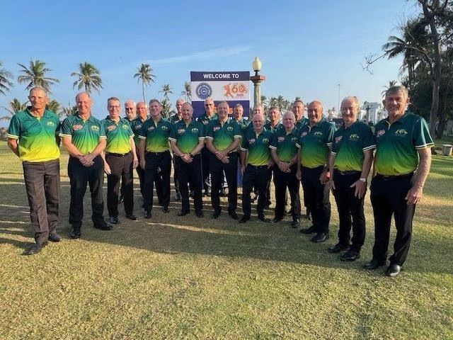 Group of men in green and gold shirts pose in front of a sign