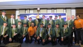 Group of men in green jackets, holding a trophy indoors.
