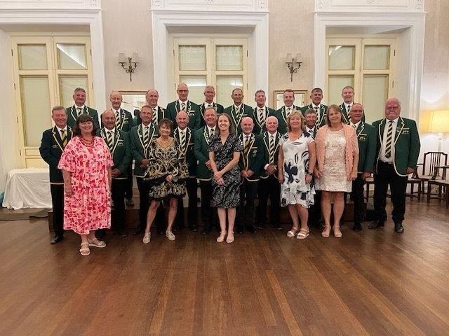 Group of people, mostly men in green jackets, posing in a room