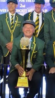 Man in green jacket and cap holding a trophy