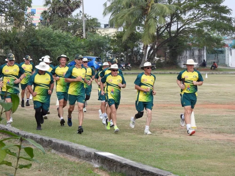 Group of people in Australian cricket uniforms running on a grassy field