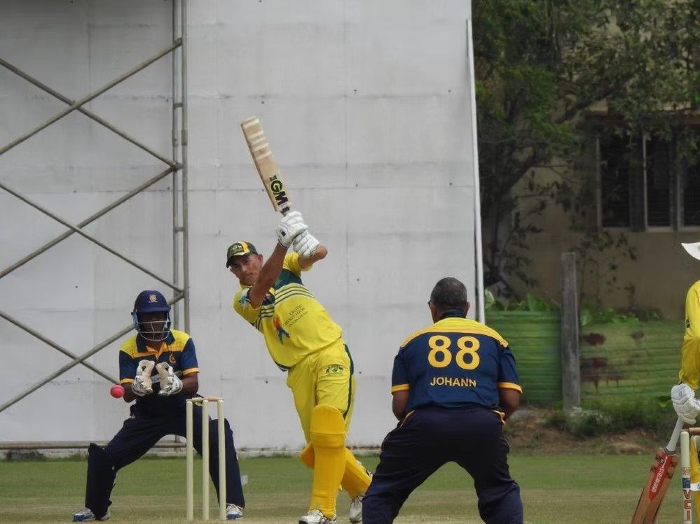 Cricketer in yellow and green uniform batting
