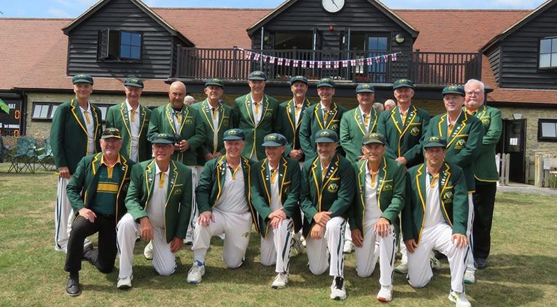 A group of men in green jackets and white pants in front of a wood building