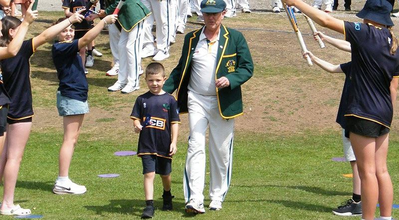 Veterans Cricket Man in green jacket and young boy walk through cheerleaders