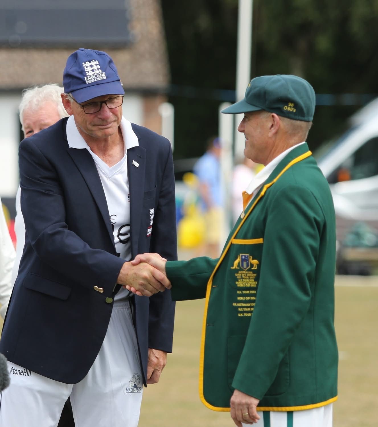 Two men shaking hands, one in a blazer and England hat, the other in a green blazer