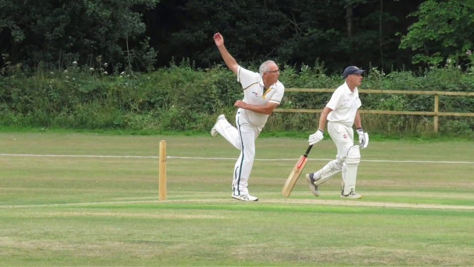 Cricketer in white uniform bowling on a green field