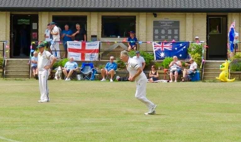 Bowler in white uniform about to bowl, batsman waits, spectators watch