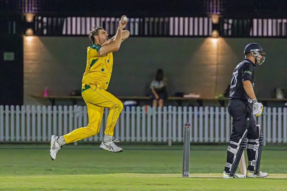 Cricketer in yellow uniform bowls a ball, batter in black gear awaits