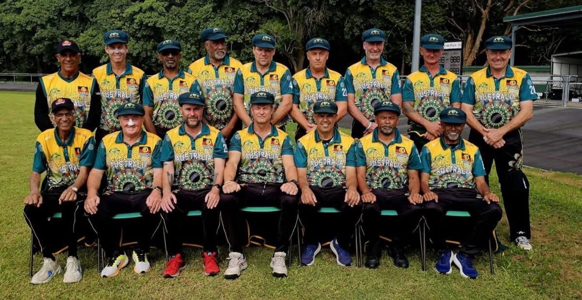 Cricket team posing outdoors in matching green and gold jerseys; grass in the foreground.