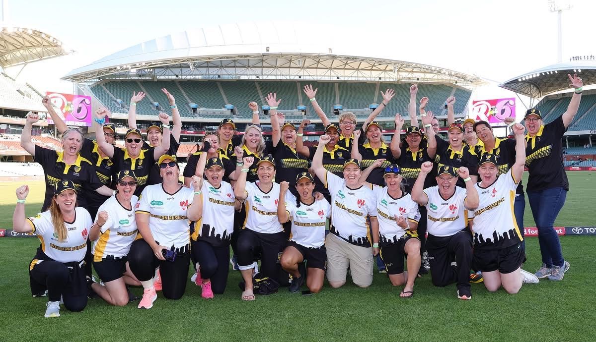 Group of people cheering on a green field, wearing black and white jerseys in front of a stadium.