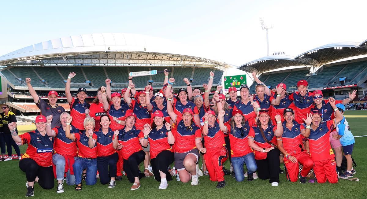 Group of people in red uniforms celebrating on a green field in front of a stadium