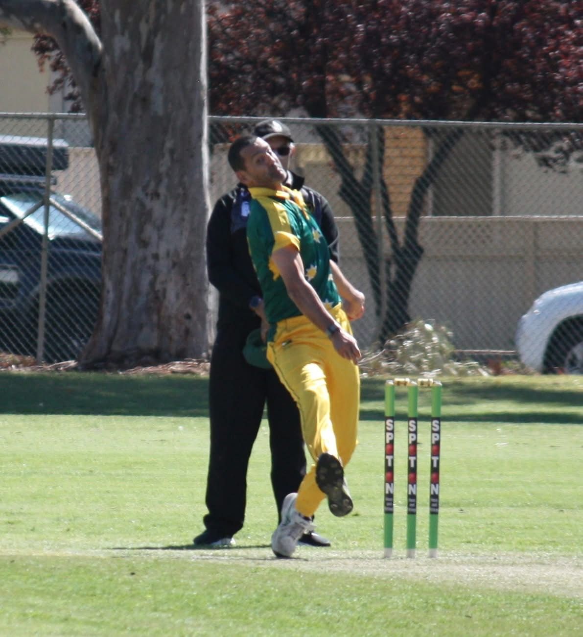 Cricket bowler in yellow and green uniform about to throw the ball