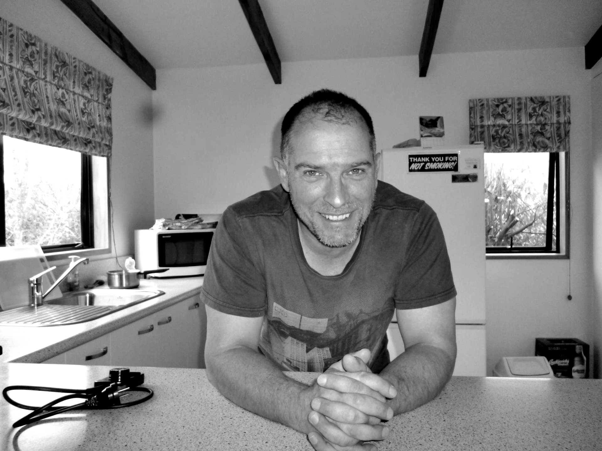 A man is sitting at a counter in a kitchen with his hands folded
