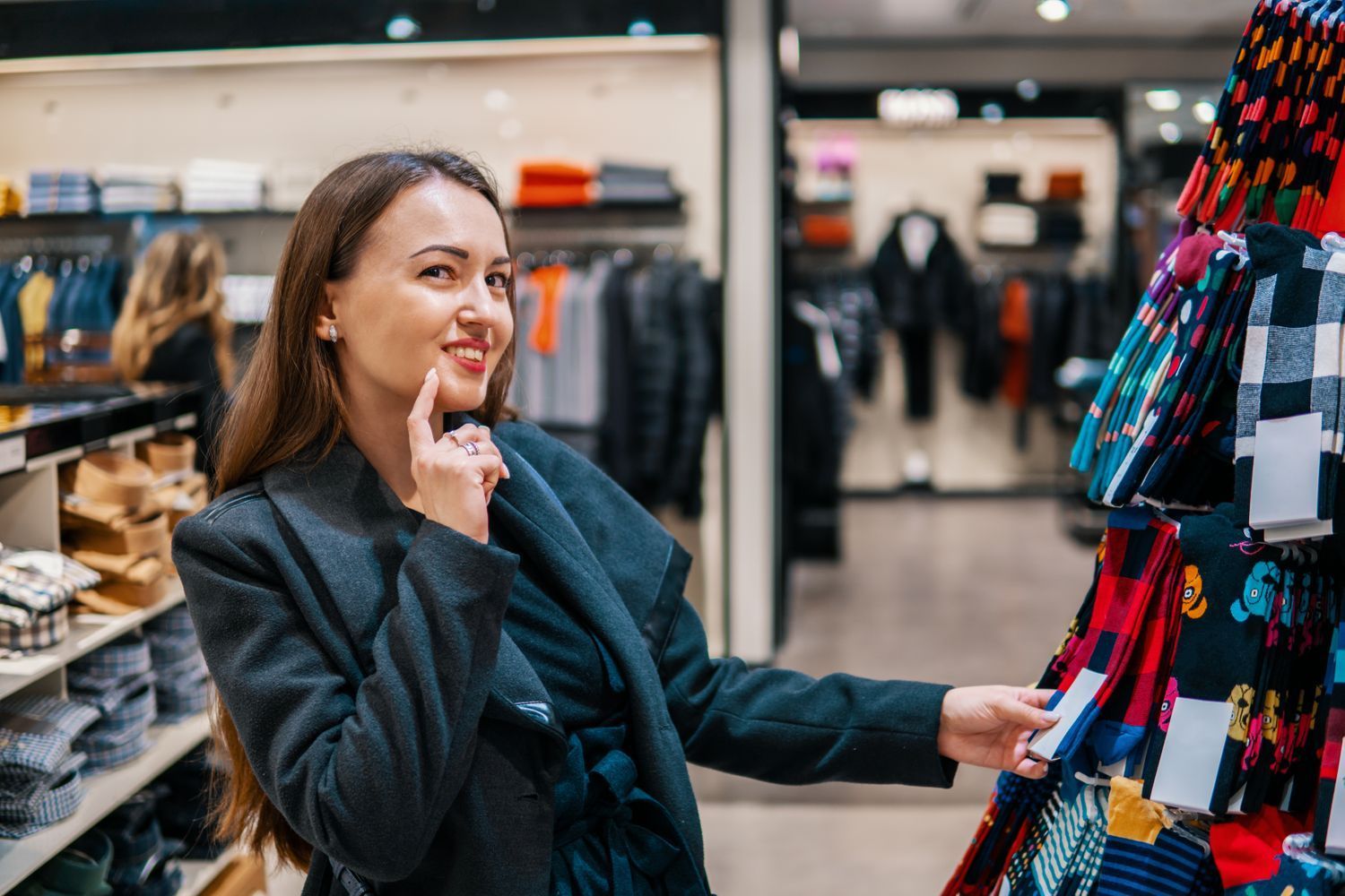 Woman shopping, smiling, looking at socks in a store, holding a price tag.