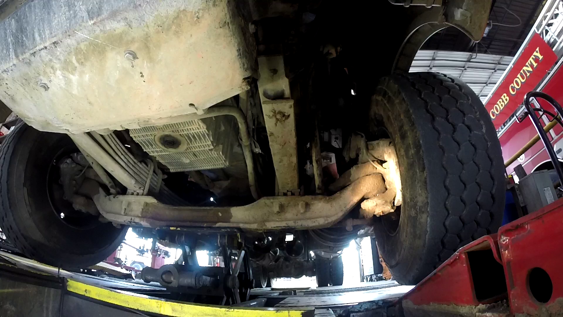 Mechanic working inside a truck, looking at engine components in a repair shop.