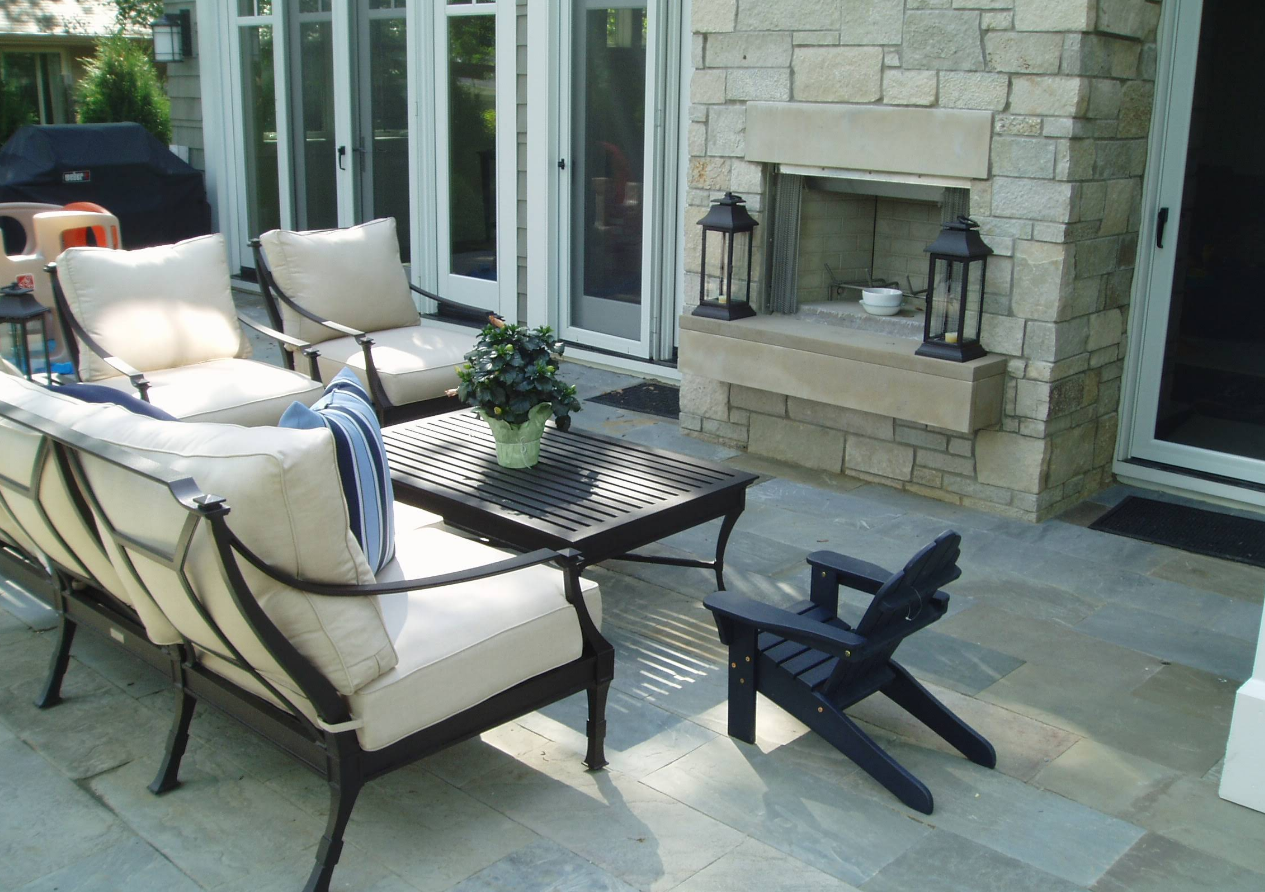 Outdoor patio with stone fireplace, seating area, and small black chair.