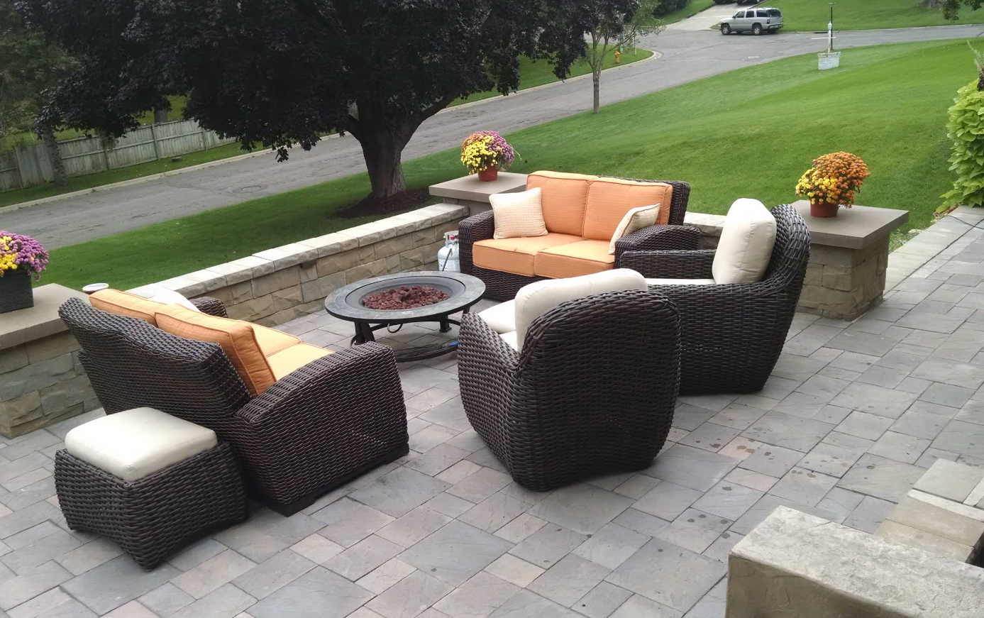 Outdoor patio with wicker furniture, including a loveseat and chairs with orange and white cushions, surrounding a fire pit.