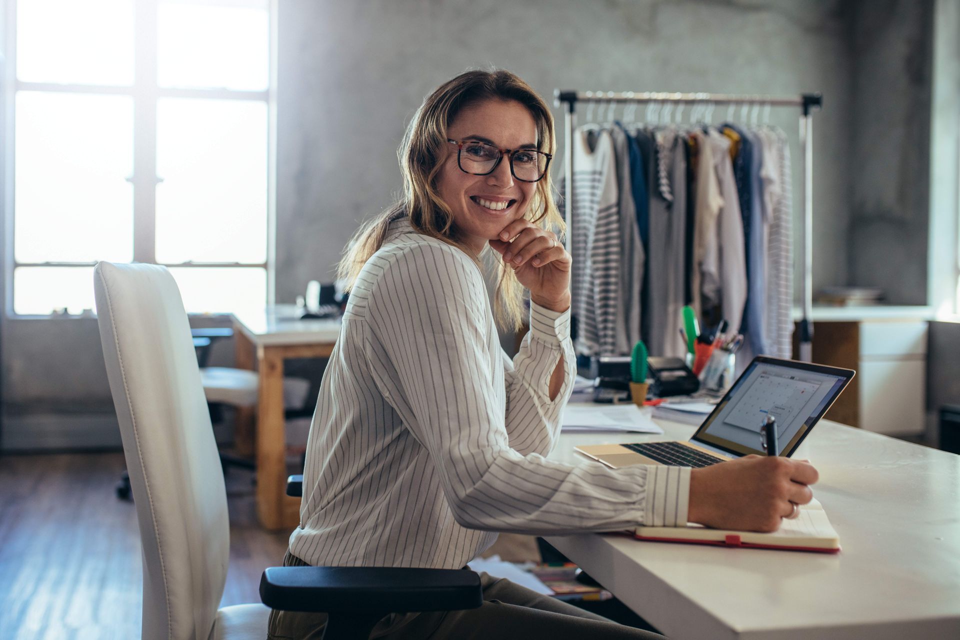 A woman is sitting at a desk in front of a laptop computer.