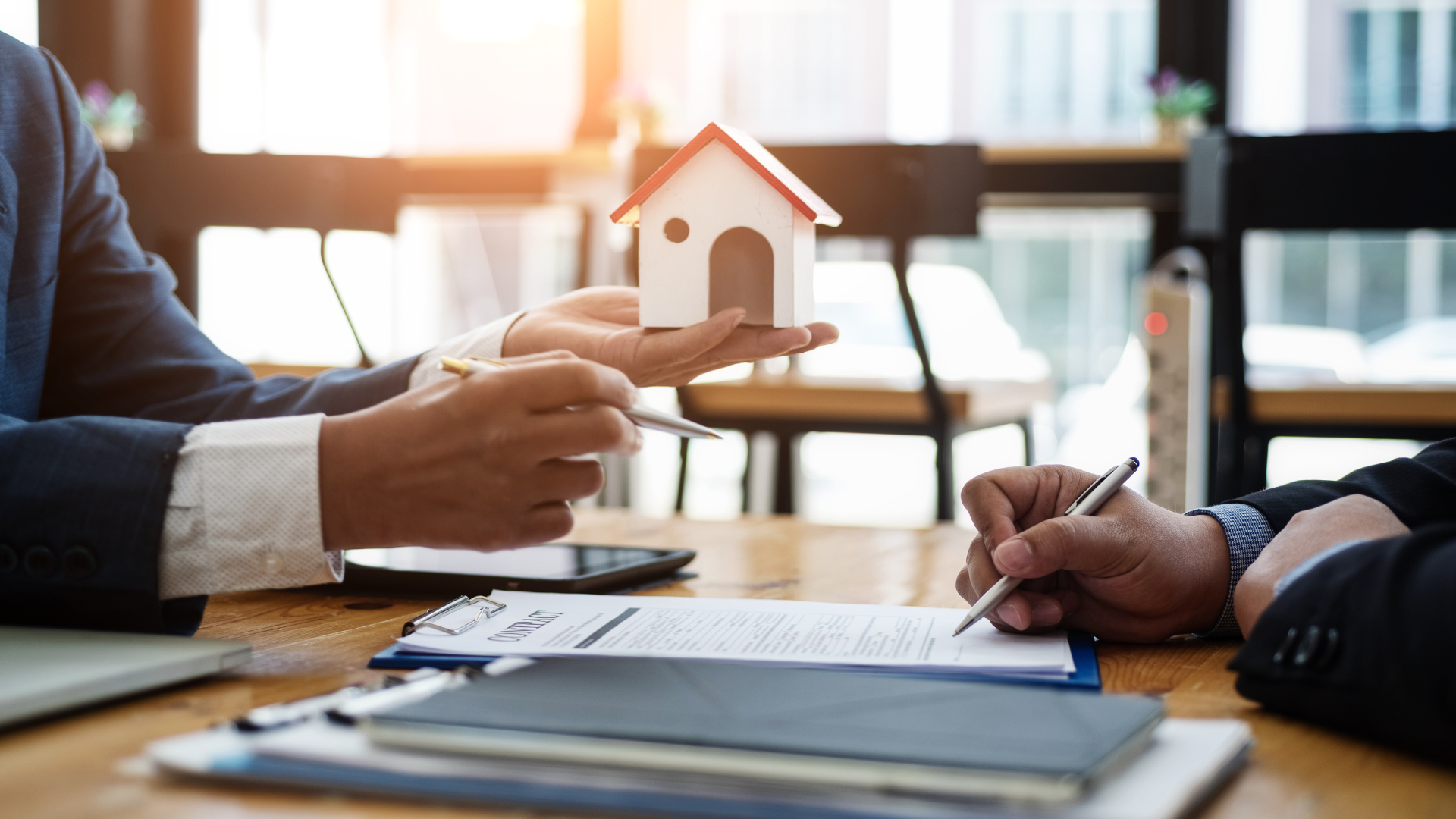 a man is holding a model house while another man signs a document .