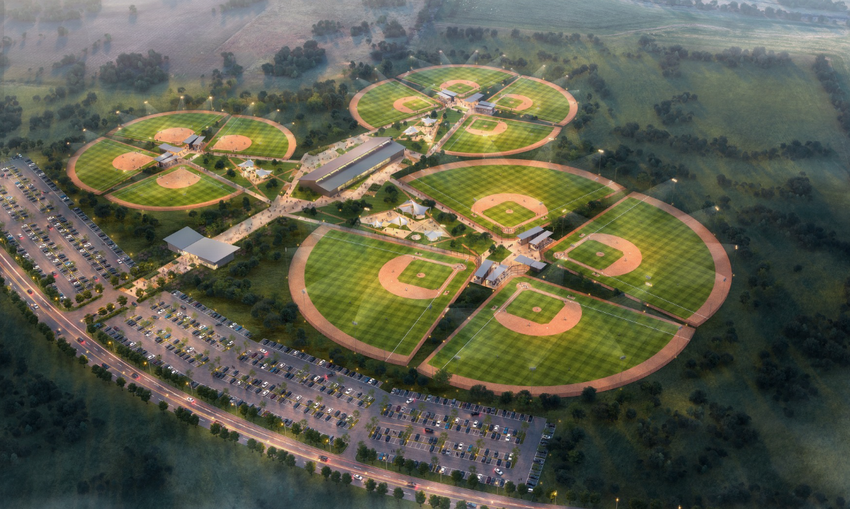 Aerial view of a baseball complex with multiple diamond fields, parking lots, and surrounding greenery.