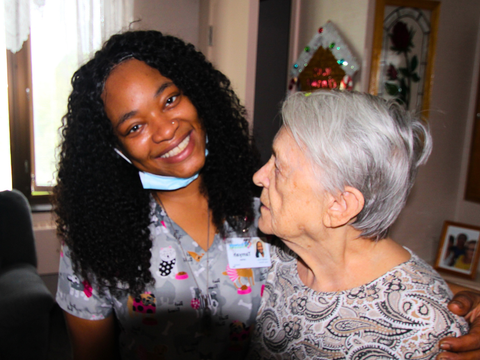 an elderly woman in a wheelchair is talking to a nurse who is wearing a red jacket that says nursing care